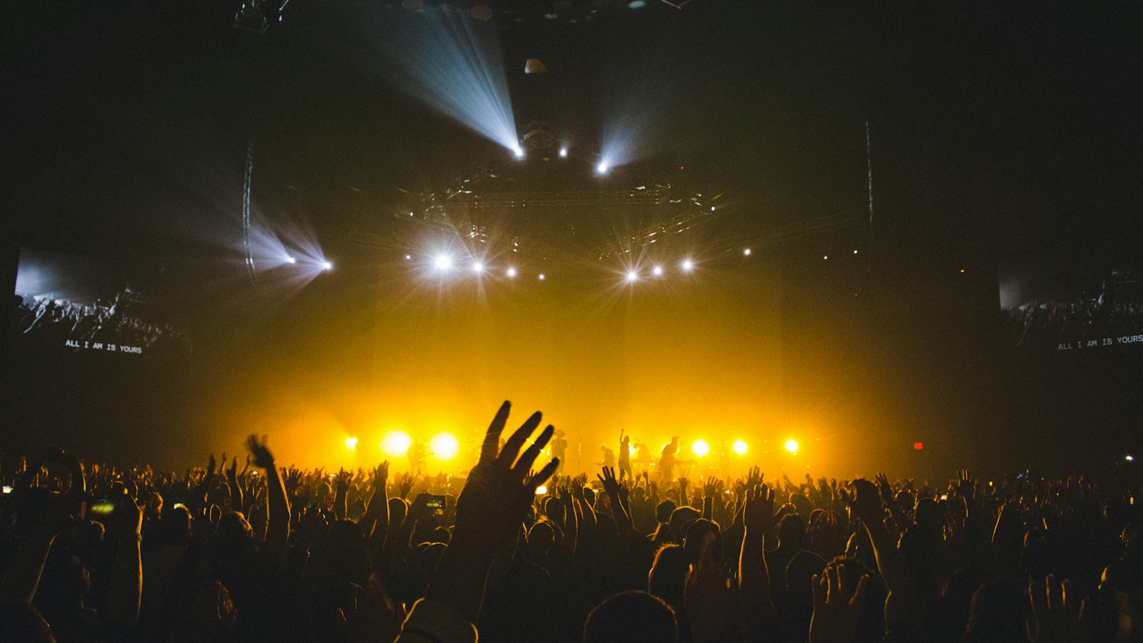 A crowd with raised hands at a concert under stage lights
